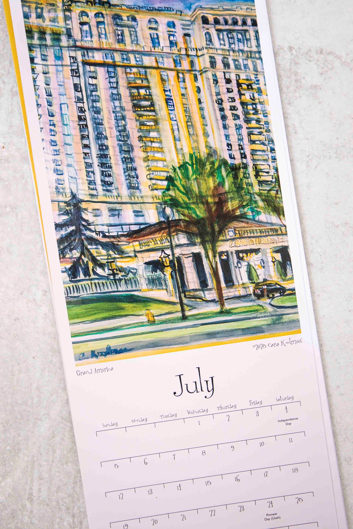 Calendar page for July with a watercolor painting of a city street and buildings.