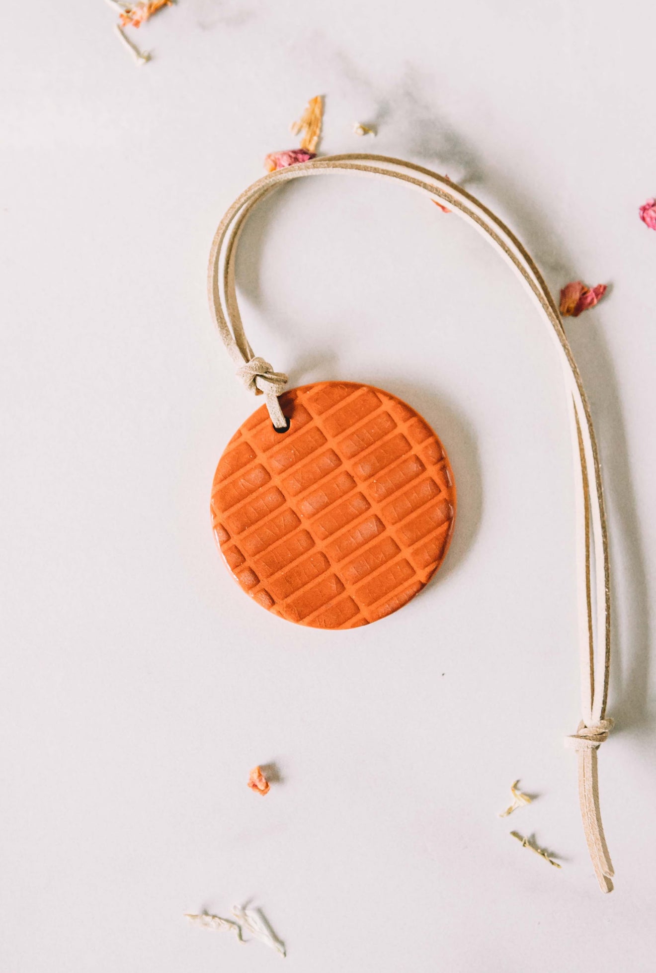 Orange, round clay car diffuser with a leather cord