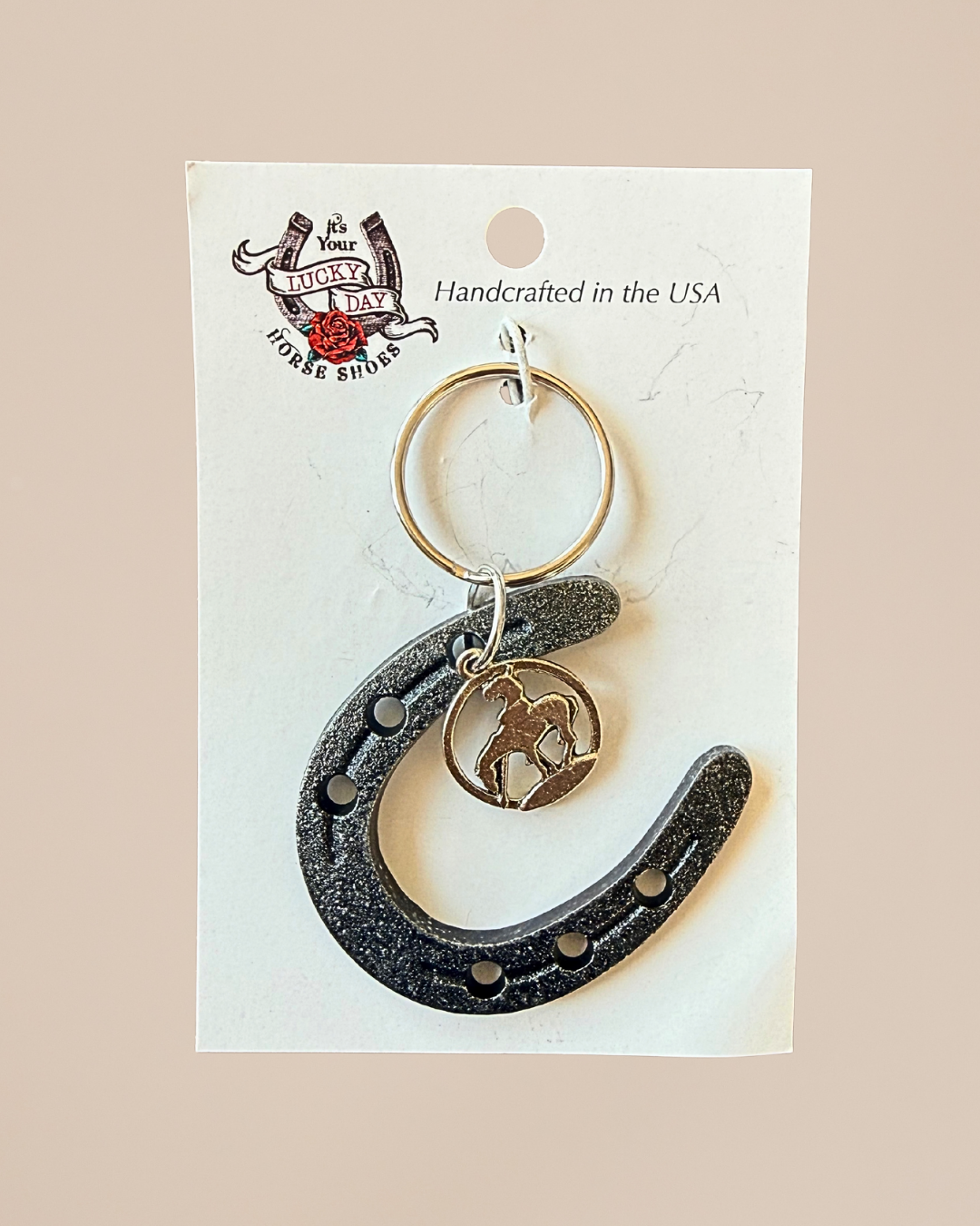 Horseshoe keychain with horse figure on a white card with branding and text.