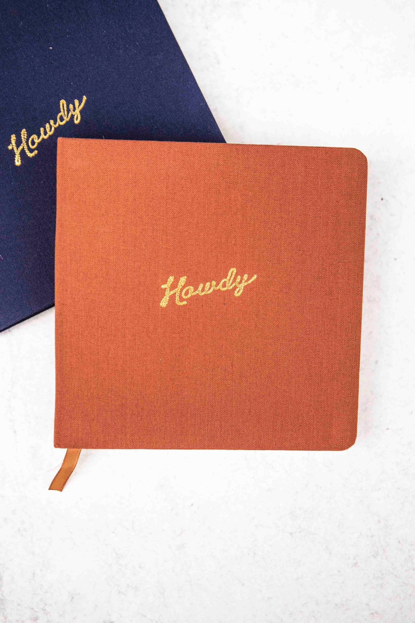 rust colored cloth notebook with 'Howdy' embroidery on a white background