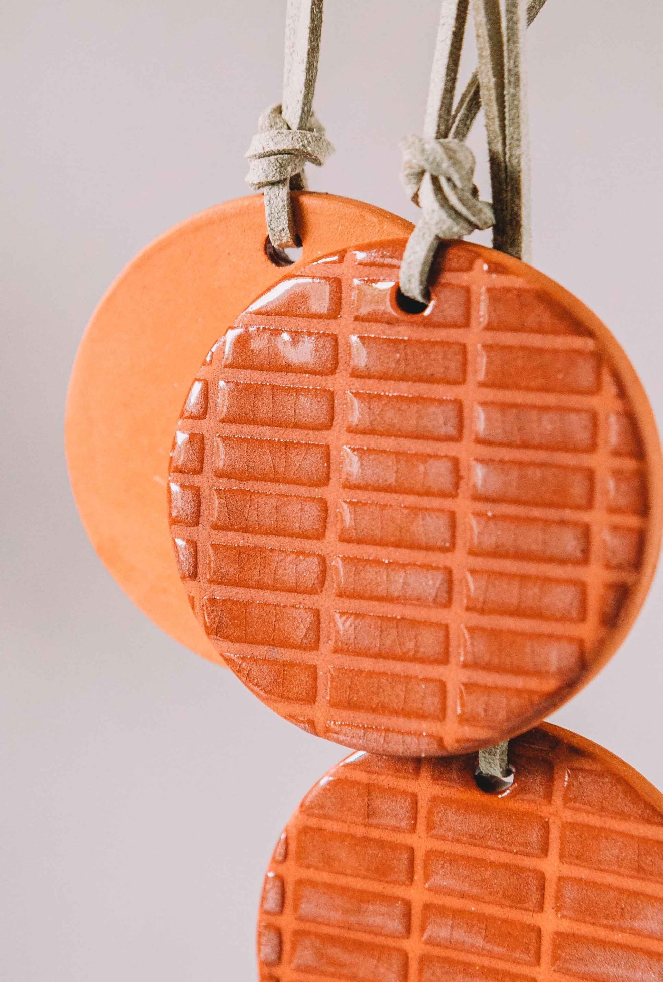 Orange, round clay car diffuser hanging on strings against a light gray background