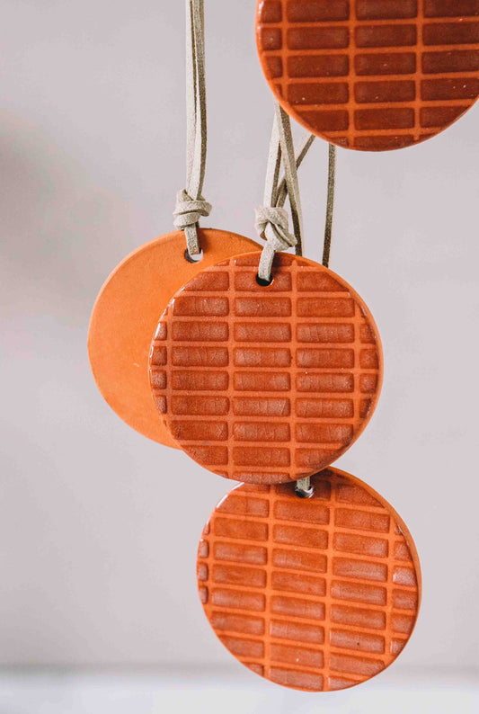 Orange clay round car diffuser hanging against a light gray background