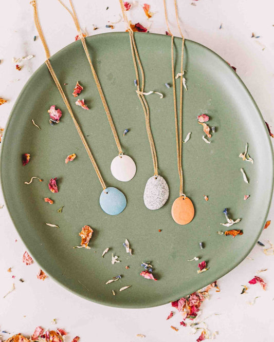 Necklaces with round pendants on a green plate with dried flowers.