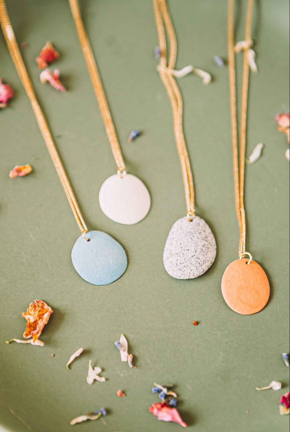Three necklaces with round, color-dyed stones on a green surface with dried flowers.