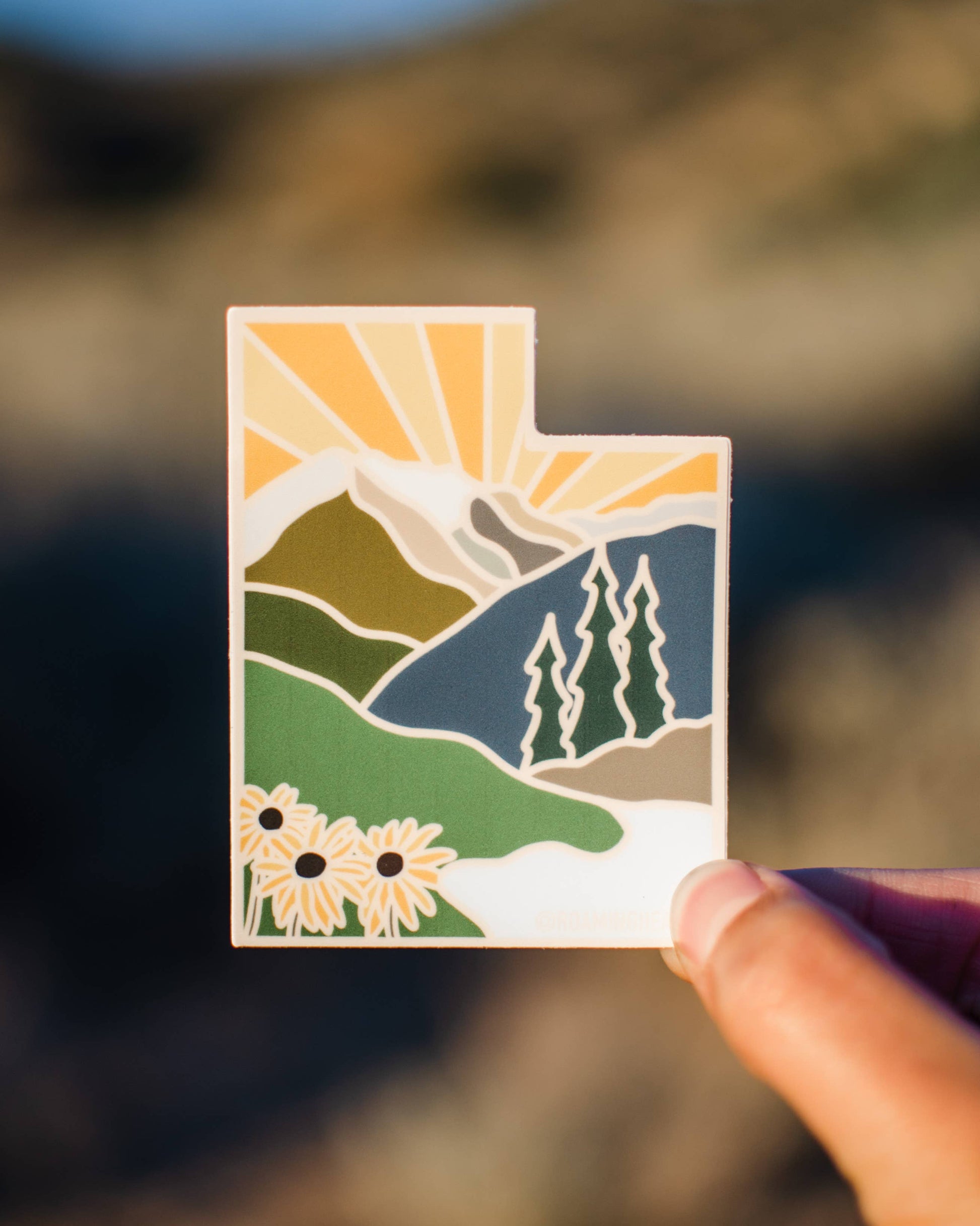 Small card with a scenic design held by a hand against a blurred natural background