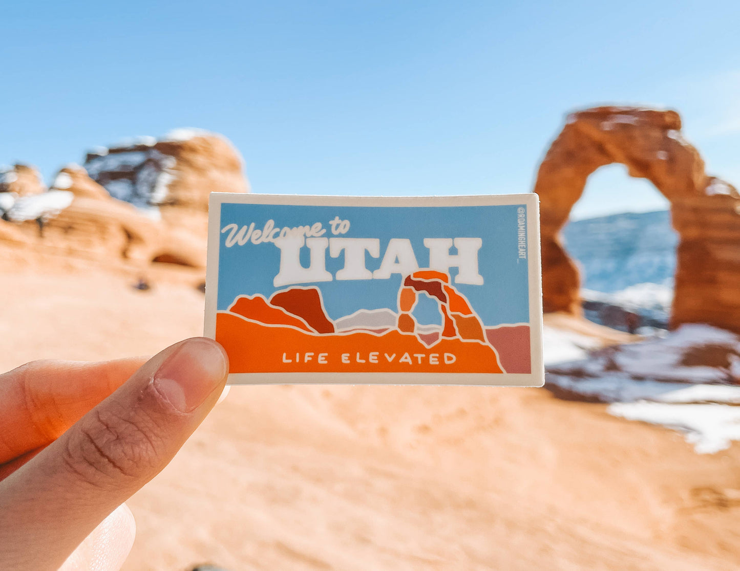 Sticker with 'Welcome to Utah' text held in front of Arches National Park