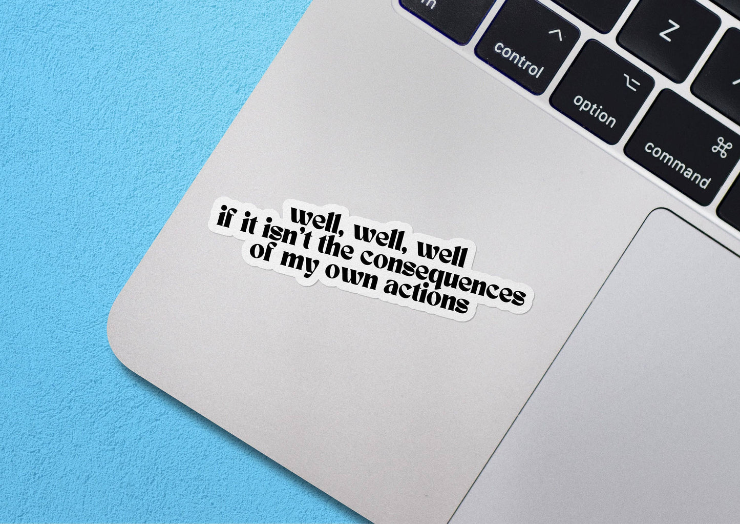 Laptop with a sticker on the palm rest area that reads "Well, Well, Well If This Isn't The Consequences Of My Own Actions" against a blue background