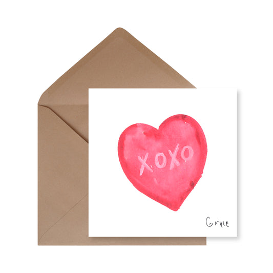 Card with red heart and 'XOXO' text, accompanied by a brown envelope on a white background