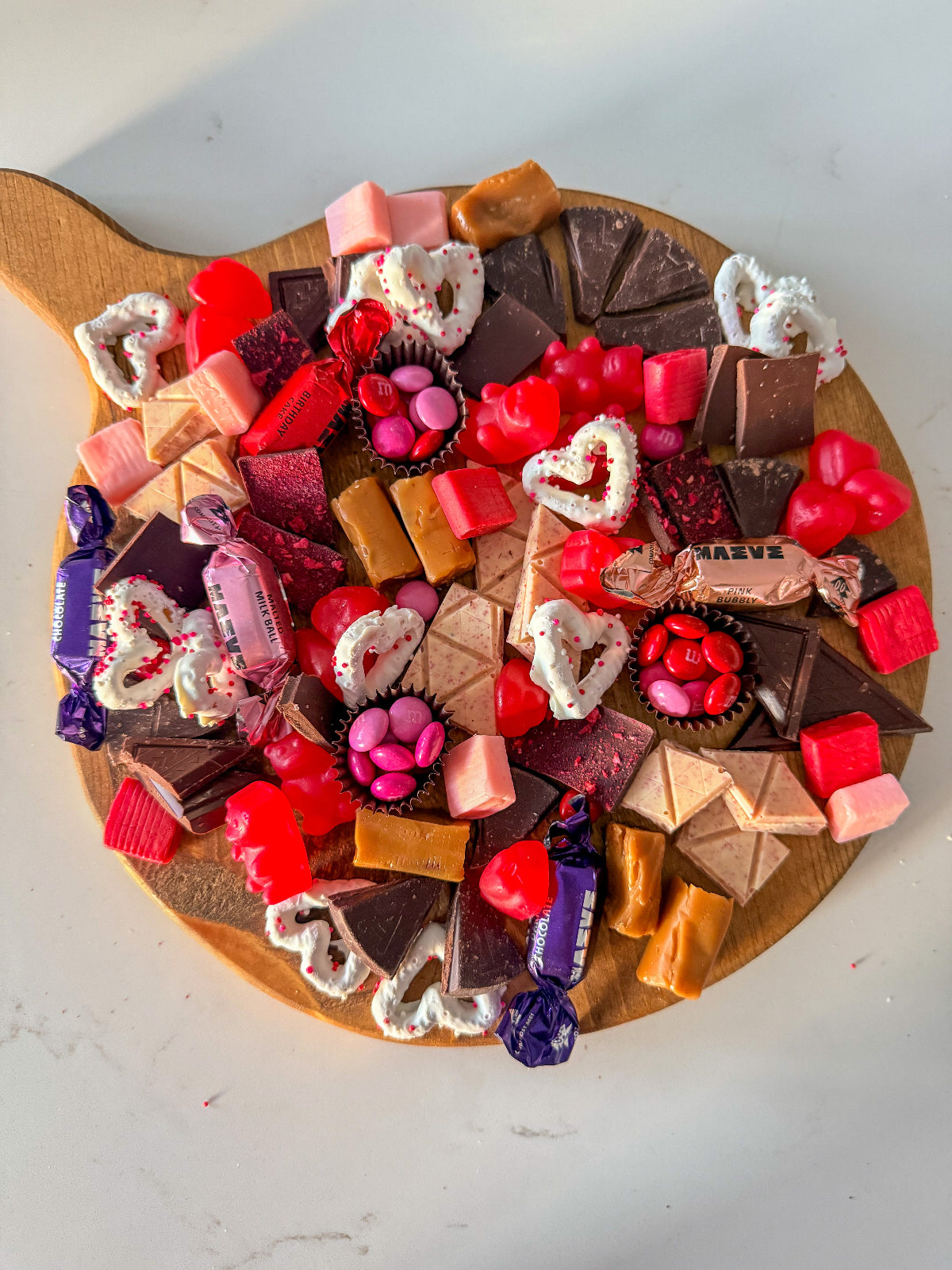 Assorted colorful candies and artisan chocolate on a wooden board with a white background