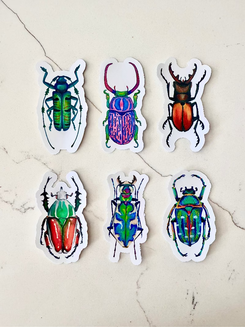 Six colorful beetle stickers on a textured beige surface