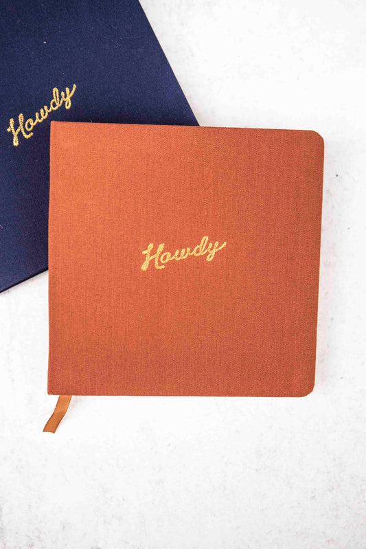 rust colored cloth notebook with 'Howdy' embroidery on a white background