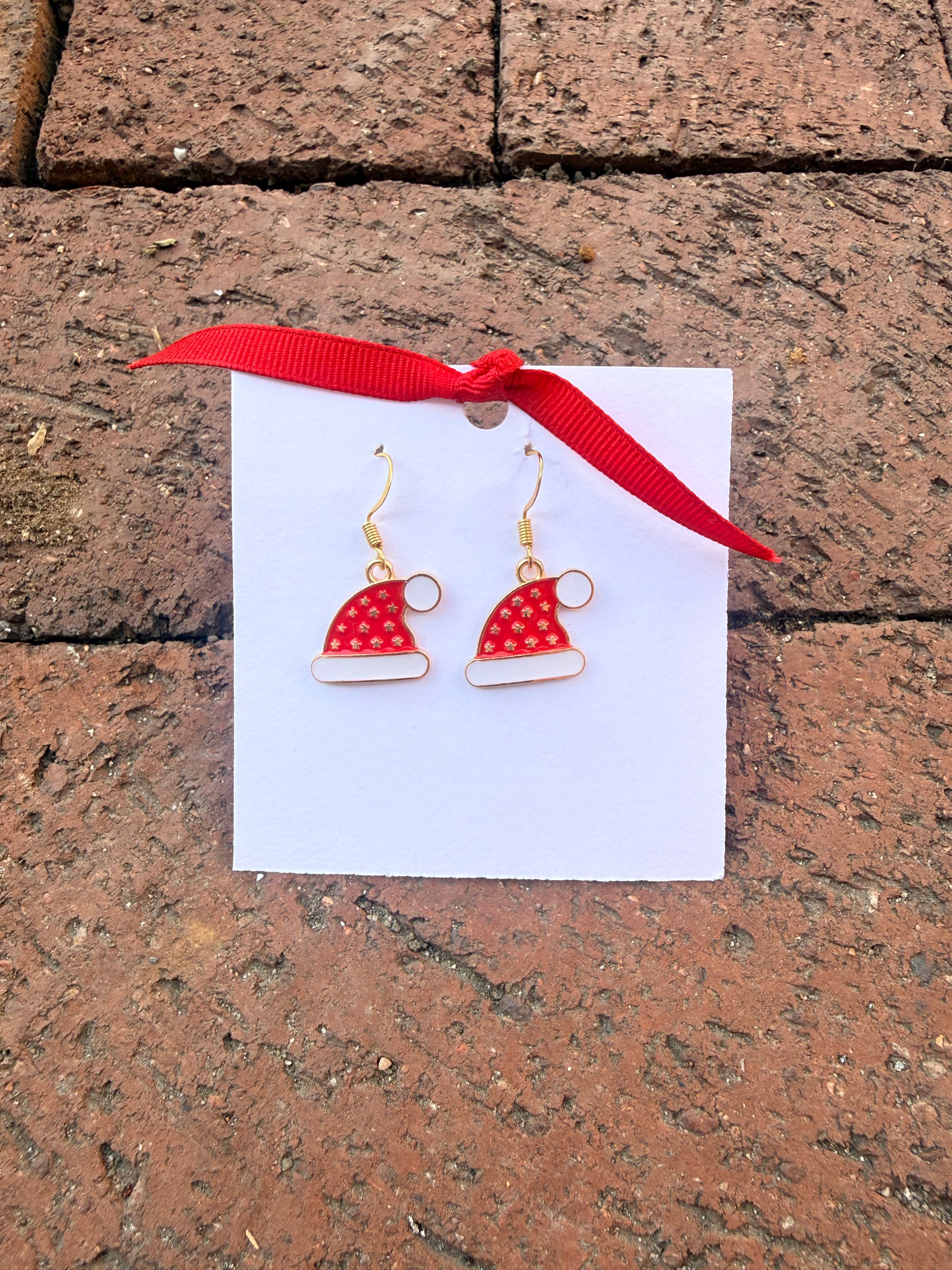 Red and white earrings on a card with a red ribbon, placed on a stone surface.