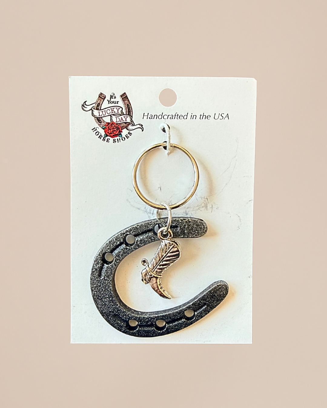 Keychain with horseshoe and feather design on a white card with branding.