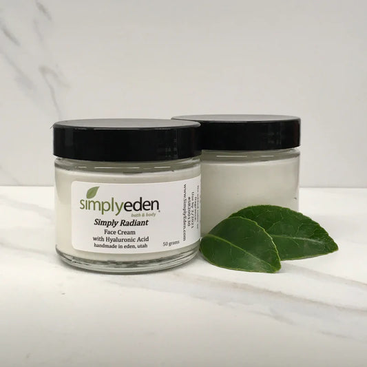 Two jars of Simply Eden face cream on a white background with green leaves.